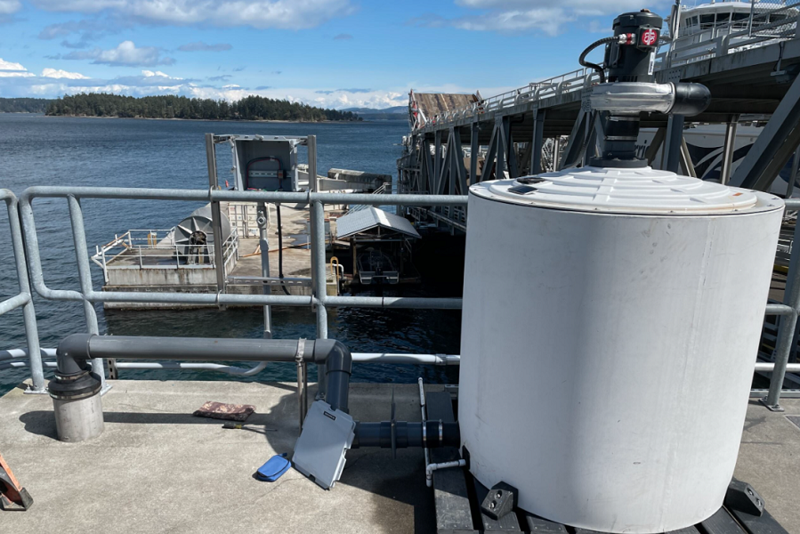 White tank on concrete slab in the foreground. Water and trees in the background.