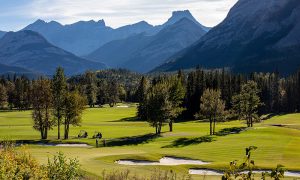 Golf course set in a mountain valley with forest and peaks in the background